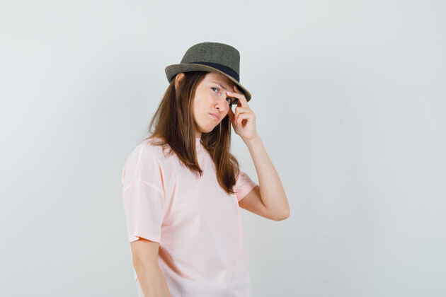 积极年轻的女性穿着粉色t恤 戴着帽子揉着太阳穴 看上去很悲伤 正面照微笑擦肖像