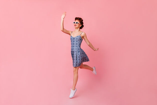 欧式戴着太阳镜的漂亮女孩挥舞着手摄影棚拍摄了一个在粉色空间跳跃的快乐的小姑娘爱情情感淑女