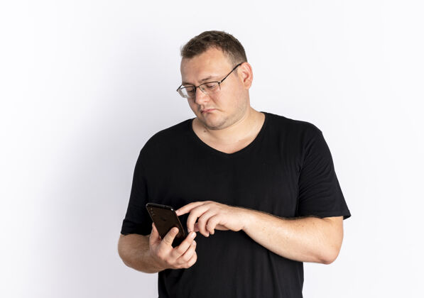 男人戴眼镜的超重男子身穿黑色t恤 站在白墙上与使用智能手机的人发短信穿用手机