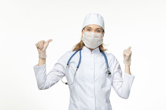 专业人员正面图女医生穿着医疗服戴着口罩和手套因白色办公桌上的冠状病毒病病毒冠状病毒-大流行性疾病正面听诊器办公桌