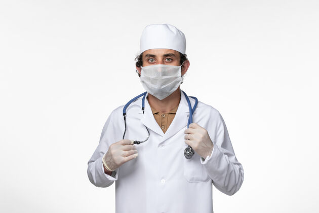 面罩正面图：男医生穿着医疗服 戴着口罩 以防白色桌上病毒的传播套装医生听诊器