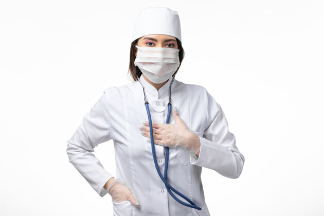 视图正面图女医生身穿白色无菌医疗服 带口罩 因白墙上冠状病毒病大流行病毒covid-女性冠状病毒预防大流行