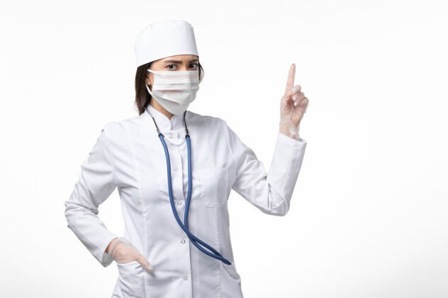 疾病正面图女医生穿着白色无菌医疗服带口罩因冠状病毒举手白墙病大流行病毒冠状病毒-实验室外套面罩病毒