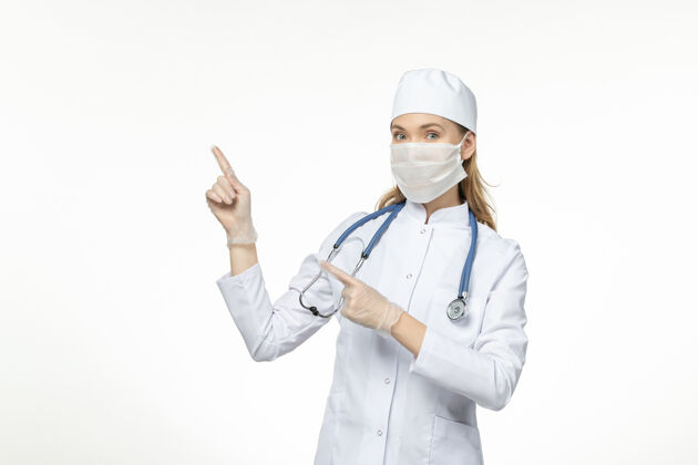 女性前视女医生身穿医疗服戴口罩因白色办公桌上冠状病毒病冠状病毒-大流行病毒病药品面罩套装