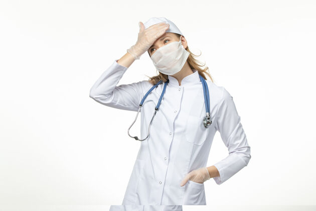疾病正面图女医生穿着医疗服 戴着口罩和手套 因白墙上的冠状病毒大流行病毒视图正面医生
