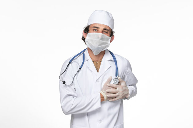 套装正面图：男医生 穿着医疗服 戴着口罩 以防在白墙飞溅病毒冠状病毒大流行时心痛喷溅冠状病毒听诊器