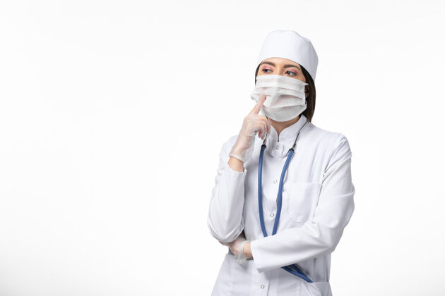 面具正面图身着白色医疗服的女医生带着口罩因冠状病毒引发对白墙健康病大流行的深刻思考人疾病思维