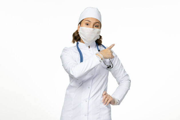 女性正面图女医生穿着白色医疗服 戴着口罩 因白墙上有冠状病毒大流行病毒病冠状病毒医学大流行人