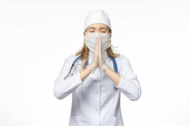 祈祷前视图女医生穿着医疗服戴着口罩和手套因冠状病毒祈祷白墙疾病大流行健康冠状病毒美丽视图人