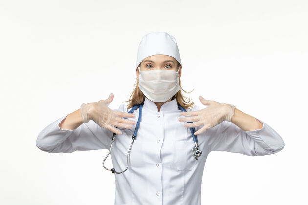 肖像正面图：女医生穿着白色医疗服 戴着防护面罩 因冠状病毒在淡白色的墙壁上传播疾病-大流行性疾病成人医学疾病