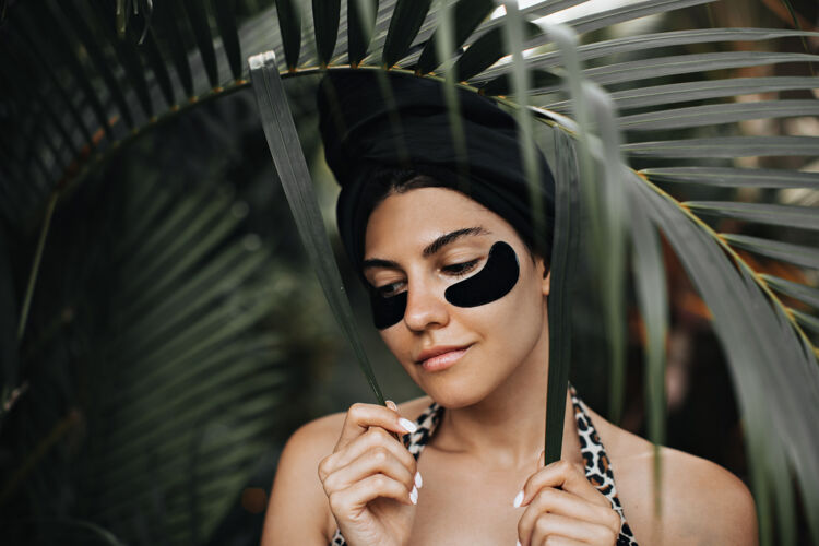 欧洲性感的女性模特 戴着眼罩 在棕榈树叶子附近摆姿势户外拍摄的迷人的戴着头巾的女人站在自然背景上年轻人自然眼罩