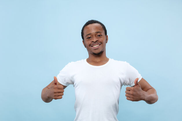 商人半身特写肖像的年轻非洲裔美国男子在白色衬衫的蓝色空间人类的情感 面部表情 广告概念显示标志og好 太好了 很好广告男人企业家