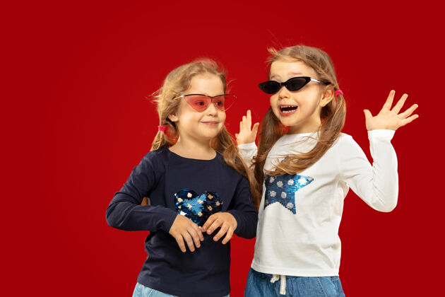 牛仔裤美丽动情的小女孩被隔离在红色空间里戴着红黑墨镜的快乐姐妹或朋友的半身肖像情绪头发长