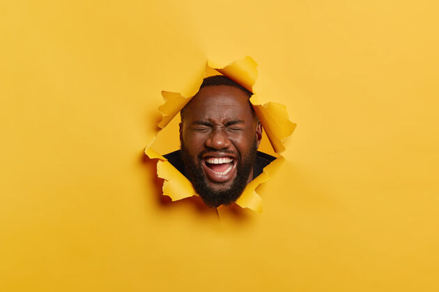 非洲黑胡子男人的头像欢笑着 觉得很有趣 在撕破的黄色背景中摆姿势 有着牙齿般的微笑 洁白的牙齿牙关明亮幸福