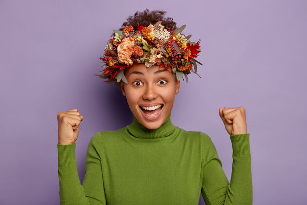 高领毛衣可爱的快乐女人的画像举起拳头 感到幸运 有热情的样子 戴着秋天的季节花环 在紫色的背景下摆姿势浆果成功高兴