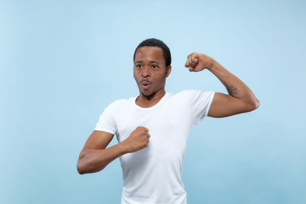 成功半身特写肖像的年轻非洲裔美国男子在白色衬衫的蓝色空间人类的情感 面部表情 广告 概念男人工作选择
