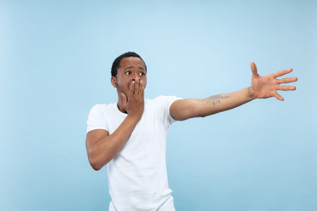广告半身特写肖像的年轻非洲裔美国男子在白色衬衫的蓝色空间人类的情感 面部表情 广告 销售理念指向 选择 惊讶男性面部衬衫