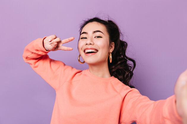 表情可爱的韩国女子与和平标志合影在紫色背景上自拍的亚洲年轻女子积极兴奋女人