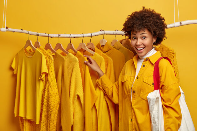 毛衣快乐的女购物狂在自己的衣柜里挑选衣架上的衣服 穿着鲜艳的夹克 拎着包 有着动人的微笑购物狂悬挂电子商务