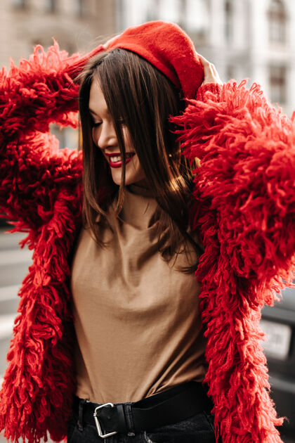 红唇穿着米色上衣和红色外套的时髦女人戴上法式贝雷帽 在城市里走来走去成功时尚红色夹克