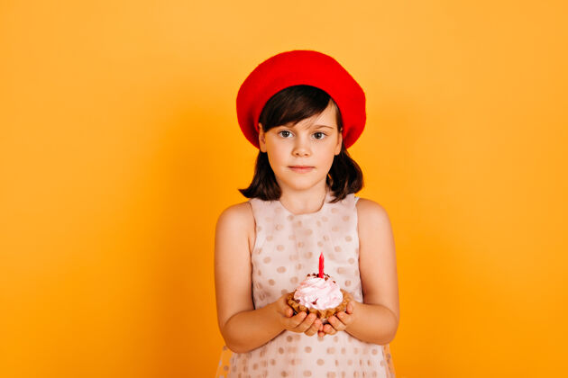 配件快乐的孩子在法国贝雷帽庆祝生日欣喜若狂的未成年少女把蛋糕孤立在黄色的墙上庆祝黑发火焰