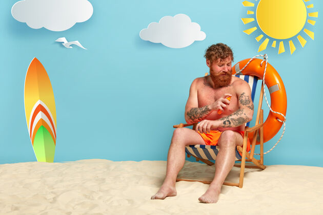 男性满脸胡须的红头发在沙滩上涂防晒霜男人防晒霜泳装