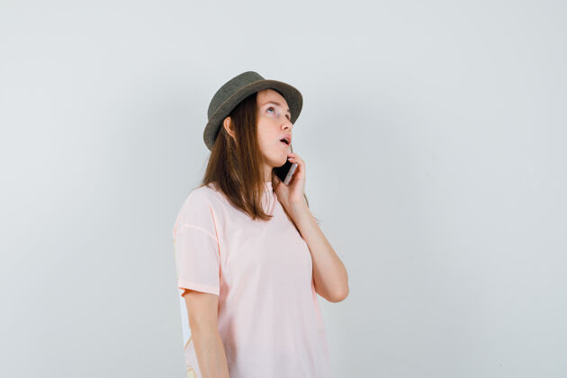 美丽穿着粉色t恤 戴着帽子 面带沉思的年轻女孩在讲手机 前视图孩子积极年轻