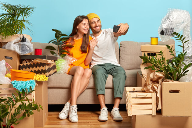 公寓幸福的年轻夫妇坐在沙发上 四周都是盒子包装自拍沙发