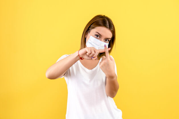 冠状病毒黄色墙壁上戴着无菌口罩的年轻女子的正视图微笑成人可爱