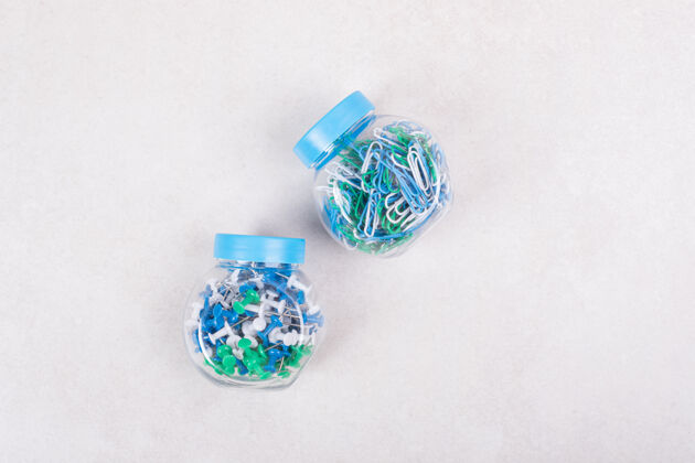 蓝色两个装满彩色别针和米黄色背景的回形针的蓝色罐子高质量照片彩色罐子元素