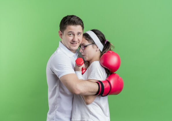 拥抱一对年轻的运动情侣戴着拳击手套拥抱着他的女朋友快乐而积极地站在绿色的墙上拳击积极站立