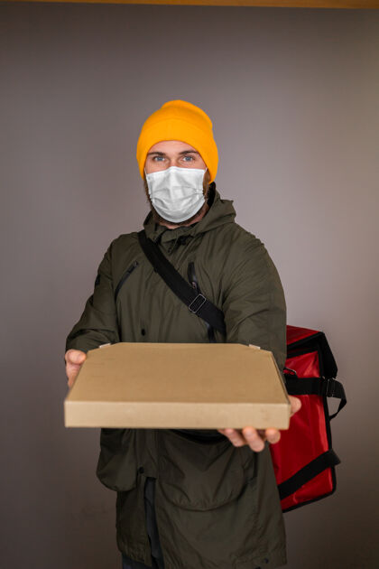 携带送一个戴着面罩的男人处理里面有披萨的纸盒 在门口给顾客快速快递微笑