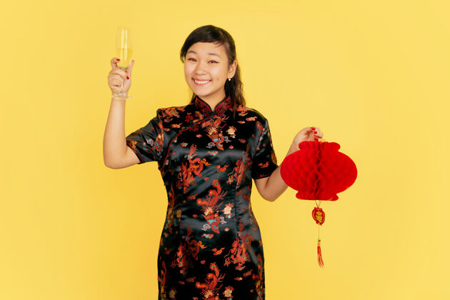 新年手持香槟和灯笼中国新年快乐黄色背景上的亚洲少女肖像身着传统服装的女模特看起来很快乐复制空间节日礼服旗袍