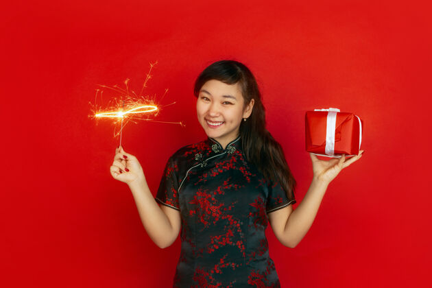 灯笼手持礼品盒和亮闪闪的火花中国新年快乐红色背景上的亚洲少女肖像身着传统服装的女模特看起来很快乐复制空间欢乐礼物祝福