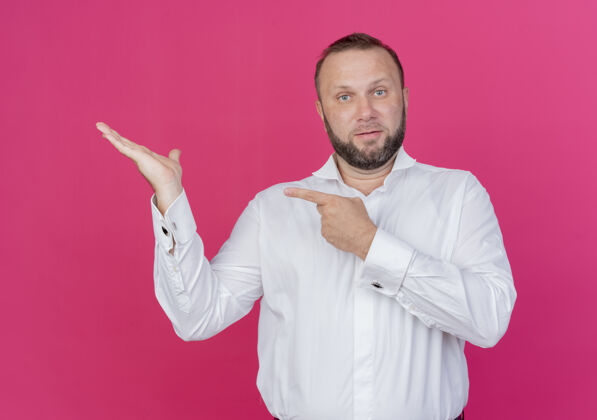 壁板一个留着胡须的穿白衬衫的男人 手上拿着一个手指指着站在粉红色墙上的一边站穿着展示