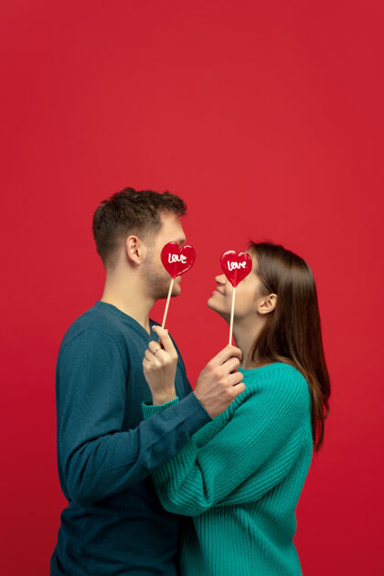 年轻美丽的情侣爱上了红色工作室墙上的棒棒糖男性微笑浪漫