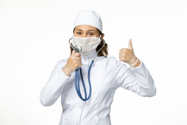 穿戴正面图年轻女医生戴防护无菌口罩因冠状病毒在白色地板上使用听诊器正面病毒听诊器