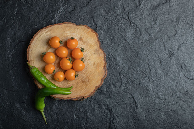 生的绿色辣椒和樱桃西红柿在黑色背景的木片上高质量的照片素食食品辣椒