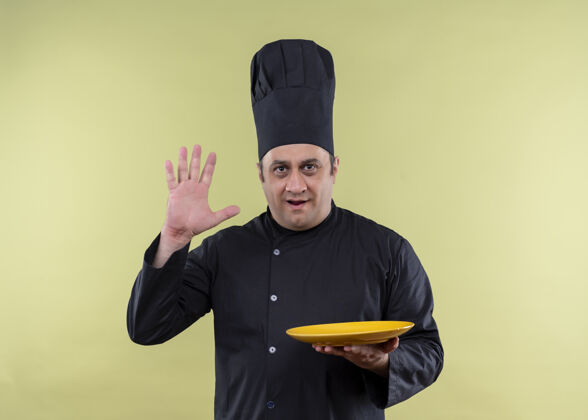 帽子男厨师身穿黑色制服 头戴厨师帽 手里拿着一个空盘子 上面有站在绿色背景上的五号手臂手臂绿色厨师