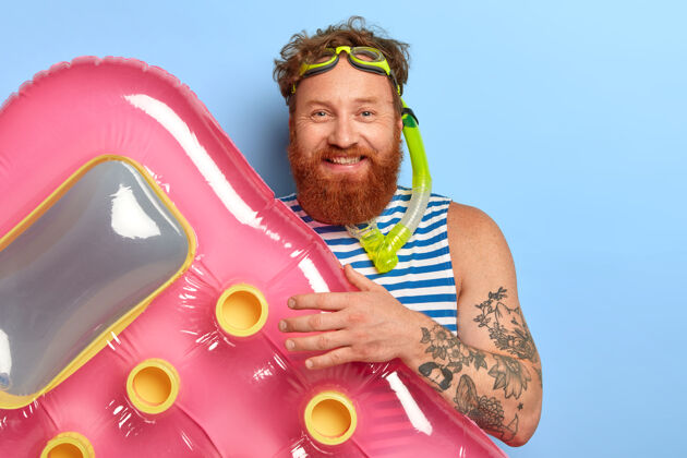 胡须积极帅气的男旅行者积极地过暑假 用充气的床垫游泳 戴着潜水面罩 留着红色的卷发和胡须 开心地笑着红发设备床垫