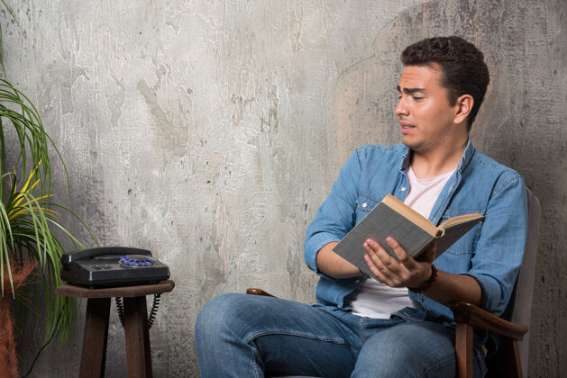 人年轻人拿着书看电话 坐在大理石背景的椅子上高质量的照片椅子电话小伙子