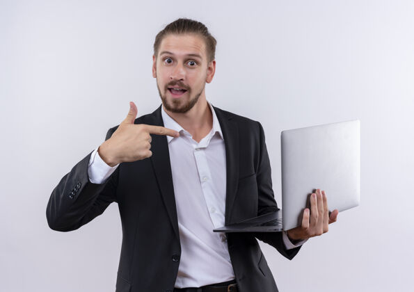 西装穿着西装的帅哥拿着笔记本电脑 手指指着电脑 站在白色的背景上欢快地笑着站着商务电脑