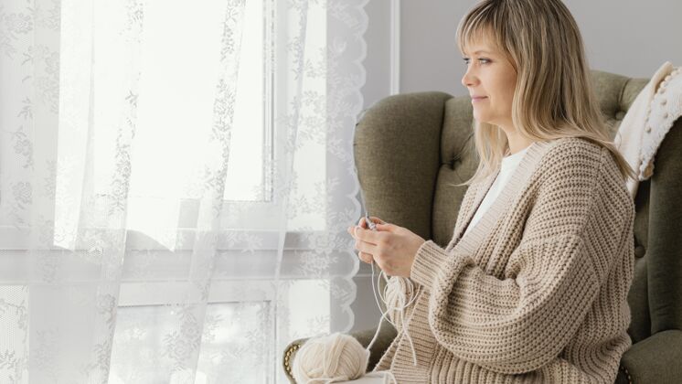 爱好中等身材的女人在窗边织毛衣女人创意纱
