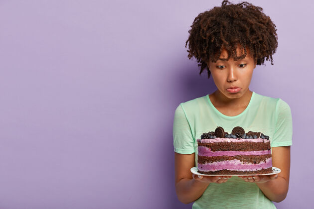 不满意不满的美国黑人妇女的照片拿着一盘蓝莓甜饼 包着下唇 没有好感 想吃美味的甜点却坚持节食善意甜饮食
