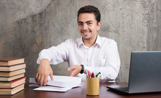 人微笑的男人拿着几张纸坐在桌子旁高质量的照片人男人办公室