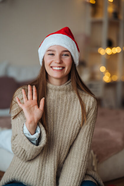 手一幅友好善良的黑发女人戴着圣诞帽向镜头挥手问好 享受圣诞节时光的画像帽子表情节日