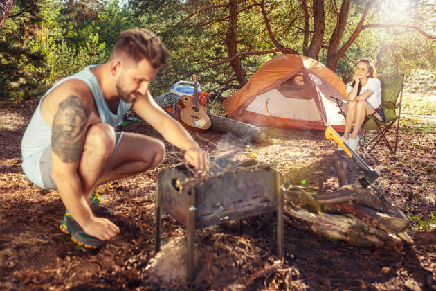 吉他聚会 男女在森林露营他们在绿草上放松度假 夏天 冒险 生活方式 野餐的概念柴火食物自然