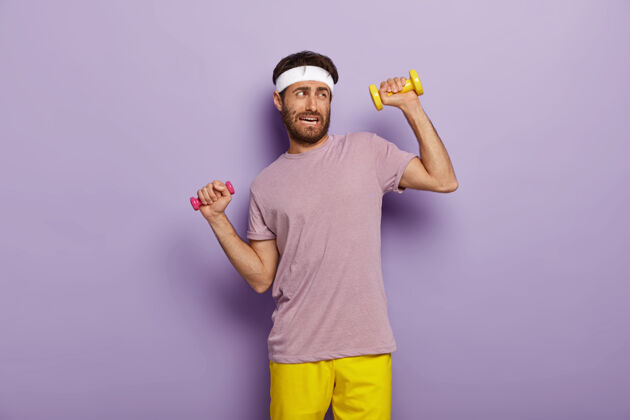 运动员疲劳和锻炼的概念不高兴的未刮胡子的男子举着哑铃 感觉疲劳的长期训练 穿着运动服肌肉健康紫色