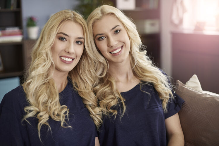 拥抱两个美丽的金发姐妹的画像沙发卷发女性