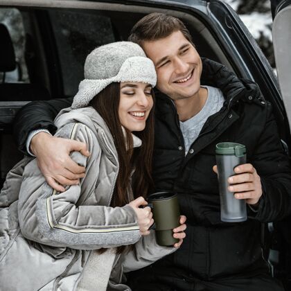 户外一对幸福的夫妇正在车的后备箱里喝热饮 而在公路旅行的前视图户外女性冒险